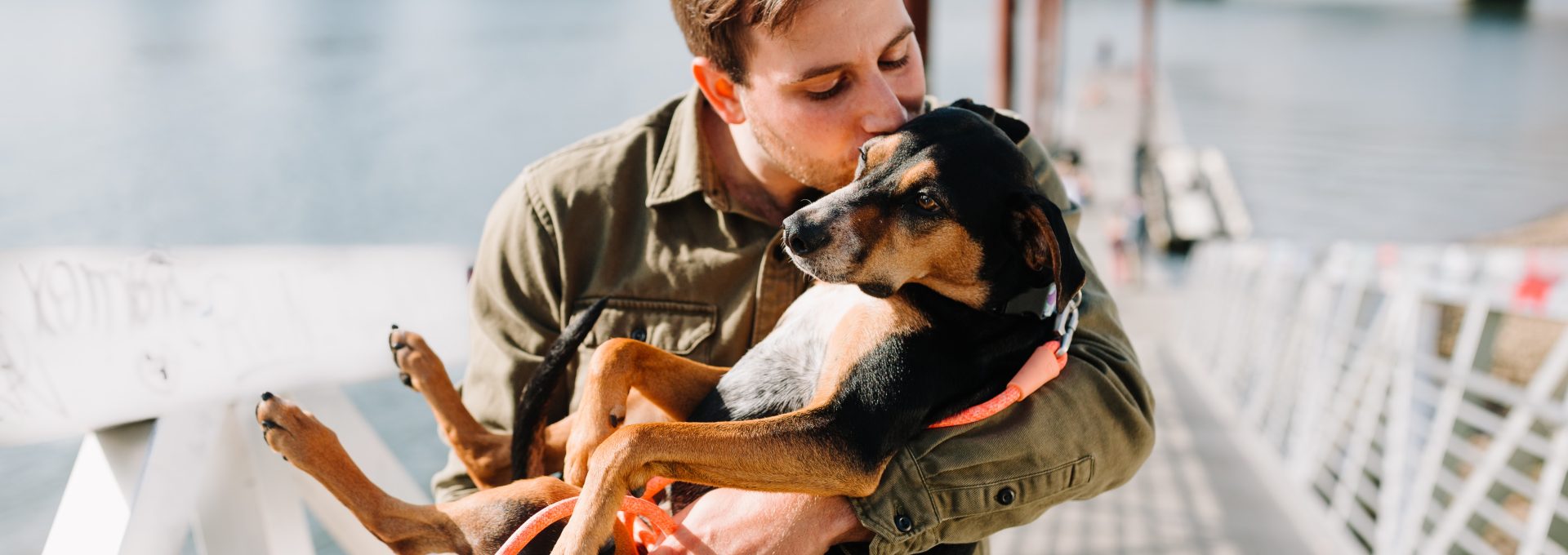 man in brown jacket hugging black and brown short coated dog