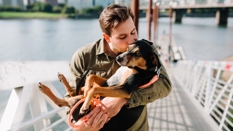 man in brown jacket hugging black and brown short coated dog
